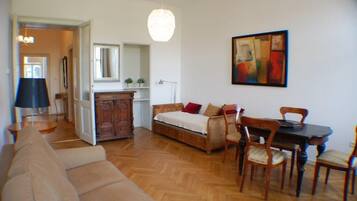 A living room with a sofa, a dining table with chairs, a wooden cabinet, and a hanging light fixture.
