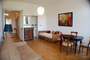 Un salon comprenant un canapé, une table à manger avec des chaises, un meuble en bois et un luminaire suspendu.