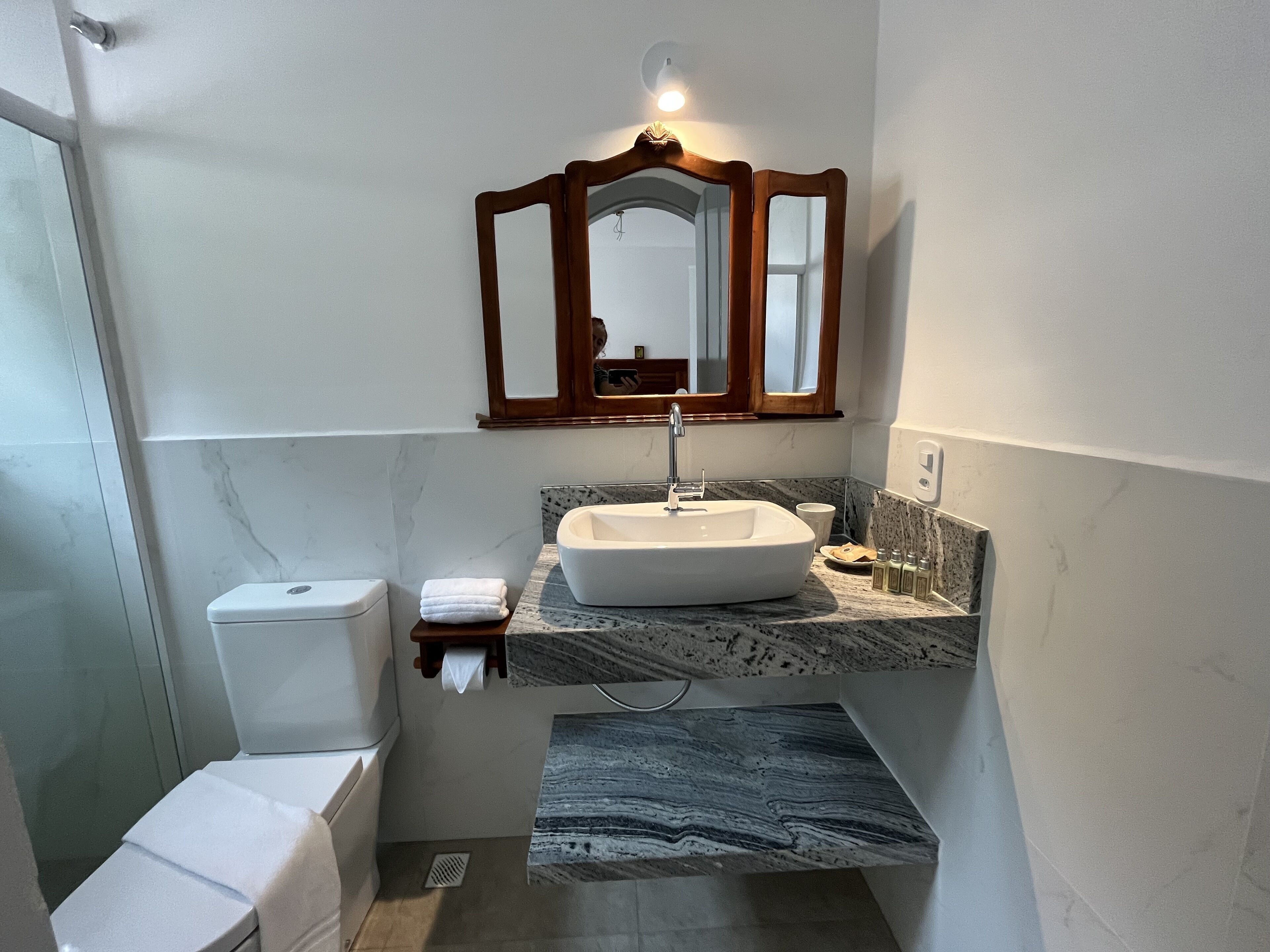 Un baño con un inodoro blanco, un lavabo con encimera de mármol y un espejo con marco de madera.