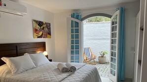 A neatly made bed with pillows and a folded blanket, a painting on the wall, and a chair outside the room. - Hotel Boutique Casa Arte Cabore (Paraty)