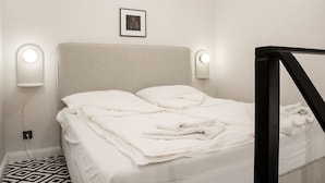 Ein ordentlich bezogenes Bett mit weißen Bettwäsche und Kissen, zwei Wandlampen und ein gerahmtes Bild an der Wand.