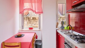 A compact kitchen with a red table, a window with a view, and a red tiled backsplash. - Lima central Old city (Dubrovnik)