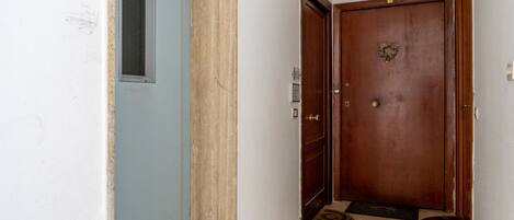 A narrow hallway with a blue door on the left, a wooden door with a brass doorknob on the right, and a small rug on the floor.