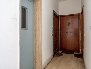 A narrow hallway with a blue door on the left, a wooden door with a brass doorknob on the right, and a small rug on the floor. - YourHome - Corso Italia Apt in Sorrento (Sorrento)