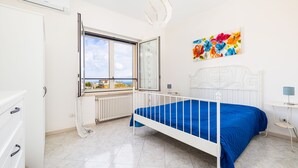 Een slaapkamer met een bed, een raam met uitzicht, een radiator en een schilderij aan de muur.