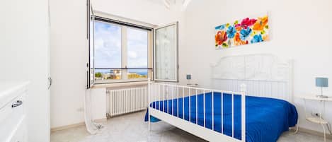 A bedroom with a bed, a window with a view, a radiator, and a painting on the wall.