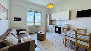 Een knus woongedeelte met een bank, een eettafel met stoelen, een keuken en een groot raam met uitzicht.