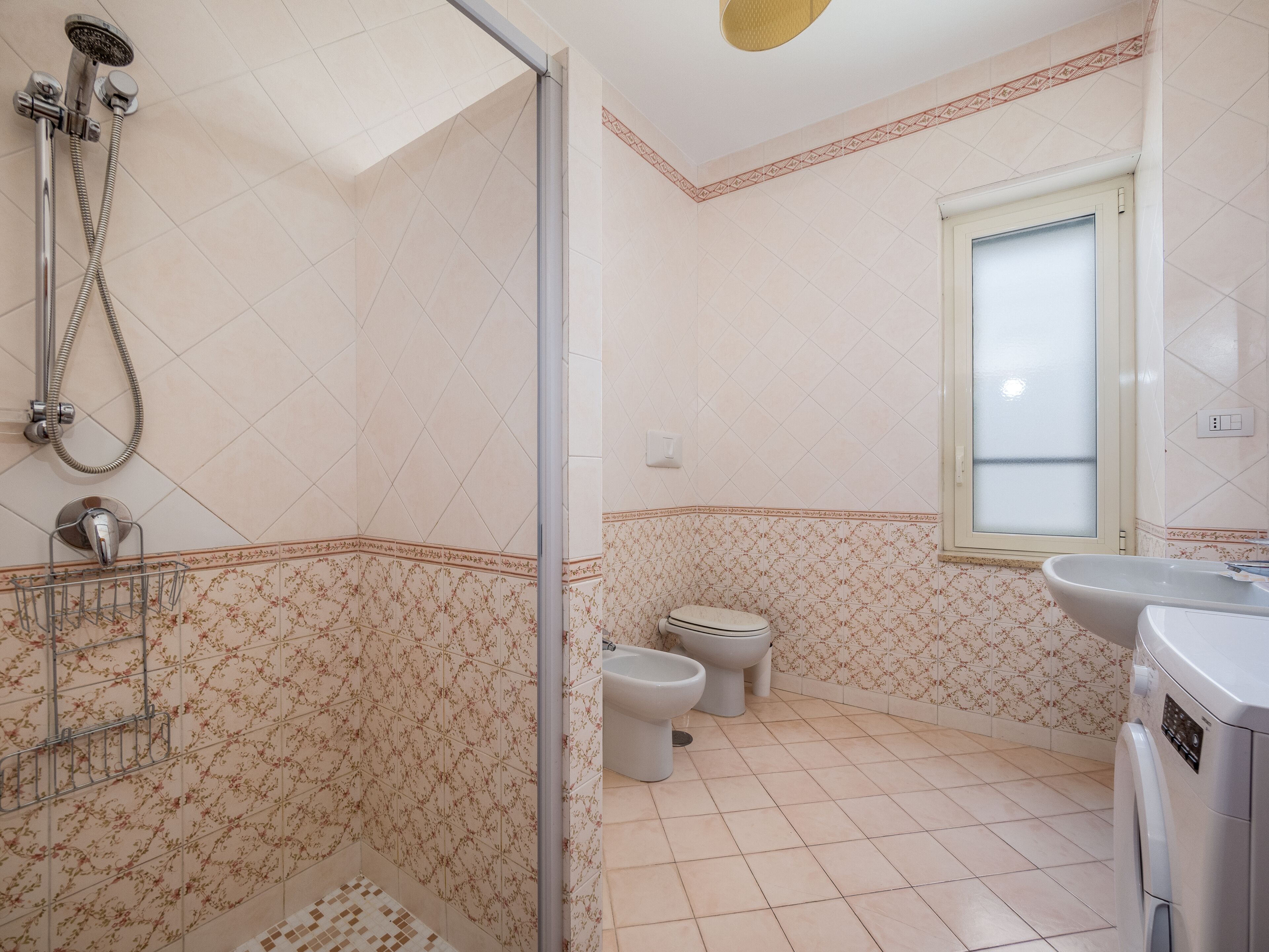 Een badkamer met een douche, toilet, bidet en een wasmachine.