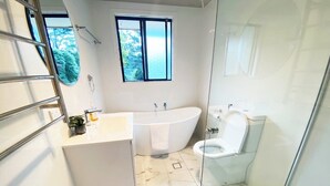 Een moderne badkamer met een vrijstaand bad, toilet en een douchecabine met glazen wanden.