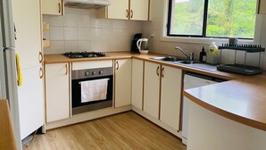 Een moderne keuken met witte kasten, een gasfornuis, een oven, een spoelbak en een raam met uitzicht op groen.