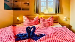 Habitación de hotel con cama, ropa de cama a cuadros, dos almohadas, ventana con cortinas, arte en la pared y lámparas de noche.