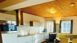 Una cocina moderna con electrodomésticos integrados, techo de madera y ventana con cortinas.