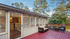A covered outdoor deck with a red floor, a sliding glass door leading to a kitchen, and outdoor furniture. - Spacious Smyrna Retreat with 3 Kitchens for Groups (Smyrna)