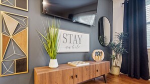 A modern living room with a wooden console table, a framed motivational quote, a television, and decorative wall art. - Spacious Smyrna Retreat with 3 Kitchens for Groups (Smyrna)