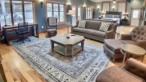A spacious living room with a large rug, a sofa, a coffee table, and a desk with a chair. - Rock House Cave Side Suite VIP Parking Cave Access (Eureka Springs)