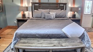 A bedroom with a large bed, two bedside tables, a bench at the foot of the bed, and a door with a stained glass window. - Rock House Cave Side Suite VIP Parking Cave Access (Eureka Springs)