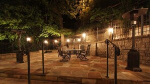 An outdoor patio area with stone flooring, a round table with chairs, and a stone wall. - Rock House Cave Side Suite VIP Parking Cave Access (Eureka Springs)