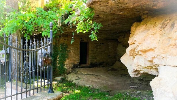 A stone archway leading into a cave-like structure with a metal gate and greenery on the left. - Rock House Cave Side Suite VIP Parking Cave Access (Eureka Springs)