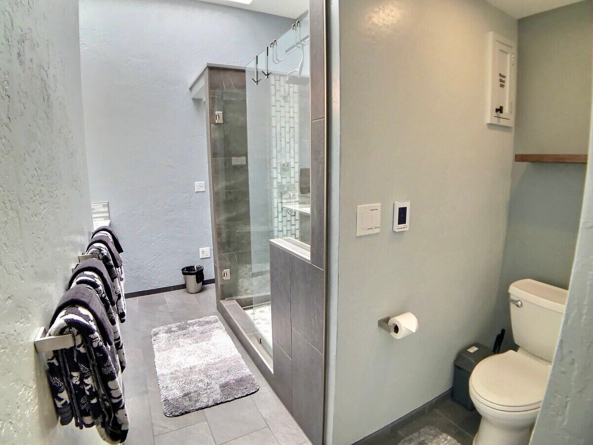 Un baño moderno con cabina de ducha de vidrio, inodoro y toallero con toallas estampadas.