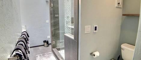 Un baño moderno con cabina de ducha de vidrio, inodoro y toallero con toallas estampadas.