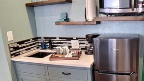 Eine kleine Küche mit Spüle, Kühlschrank, Mikrowelle und einem Regal mit Gläsern.