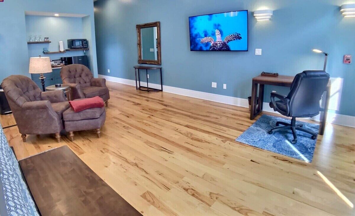 Una sala de estar con piso de madera, dos sillones, un televisor, un escritorio y una silla.
