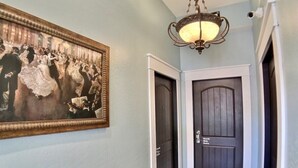 Um corredor com uma porta de madeira escura identificada como "South Side Studio", um candelabro e um quadro com dançarinos.