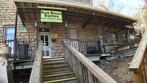 Escada levando a um edifício com a inscrição 'Rock House Suites', com uma placa indicando ser um local de hospedagem moderno no centro.