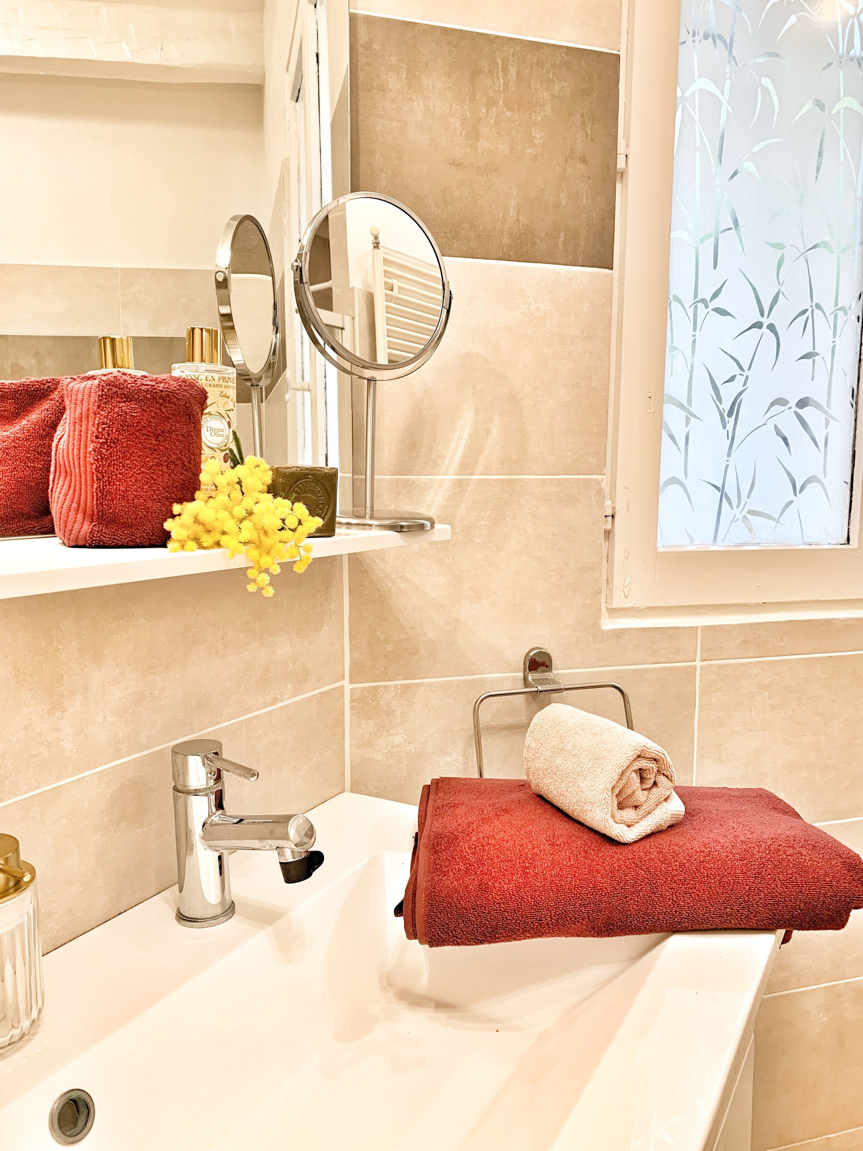 A bathroom with a white sink, a mirror, a red towel, and a window with a bamboo pattern.