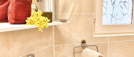 A bathroom with a white sink, a mirror, a red towel, and a window with a bamboo pattern.