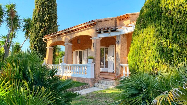 A Mediterranean-style villa with a covered porch, stone columns, and lush greenery.