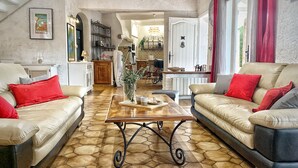 A spacious living area with a hexagonal tile floor, two sofas with red cushions, a wooden coffee table, and a view into the kitchen and dining area.