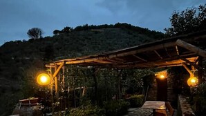 Ein rustikaler Sitzbereich im Freien mit Steinboden, Holztischen und hängenden Lampen.