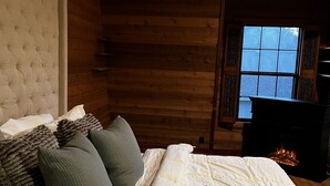 A cozy log cabin bedroom with a large bed, a fireplace, and a window with a view. - Welcome To Orlando's Chic Cabin! KING BED, FIREPLACE, SAUNA, HOT TUB, GAMES  (Sorrento)
