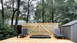 A wooden deck with two black lounge chairs and a black mattress, surrounded by a wooden fence and trees. - Welcome To Orlando's Chic Cabin! KING BED, FIREPLACE, SAUNA, HOT TUB, GAMES  (Sorrento)