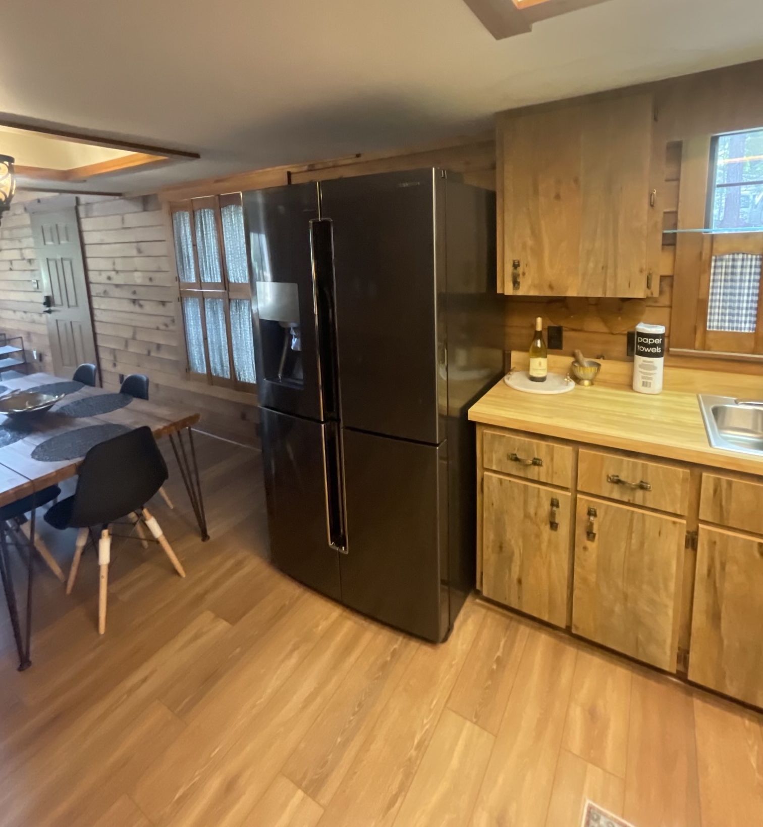 Eine moderne Küche mit Holzschränken, einem Edelstahlkühlschrank und einem Essbereich mit Tisch und Stühlen.