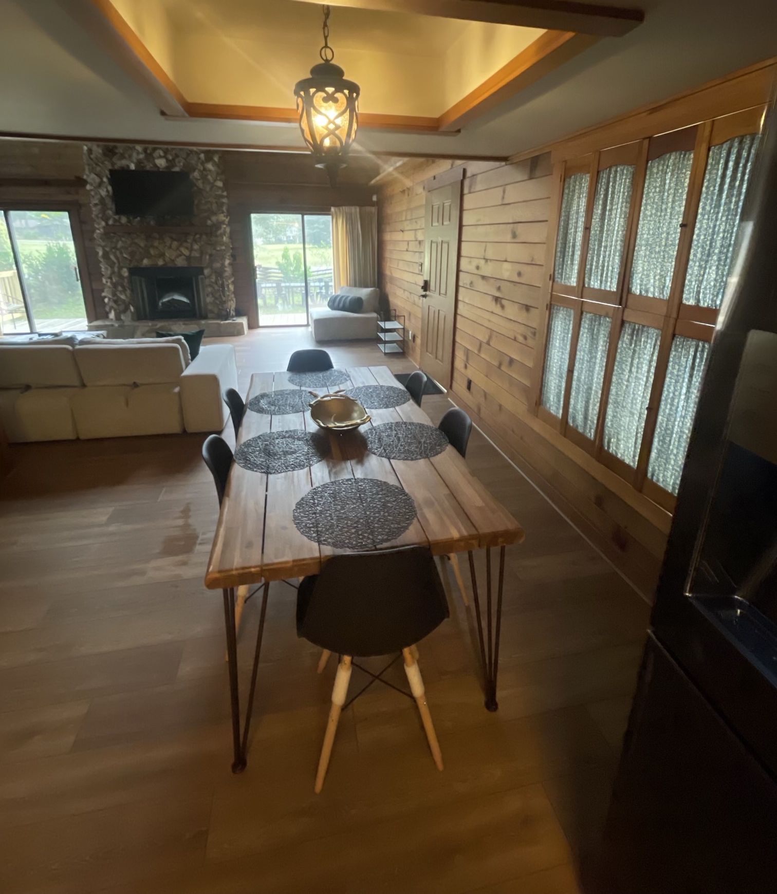 Un vaste espace dédié à la salle à manger, avec une table et des chaises en bois, une cheminée en pierre et de grandes fenêtres agrémentées de rideaux.