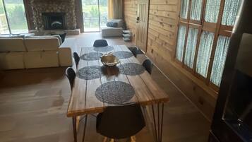Un vaste espace dédié à la salle à manger, avec une table et des chaises en bois, une cheminée en pierre et de grandes fenêtres agrémentées de rideaux.