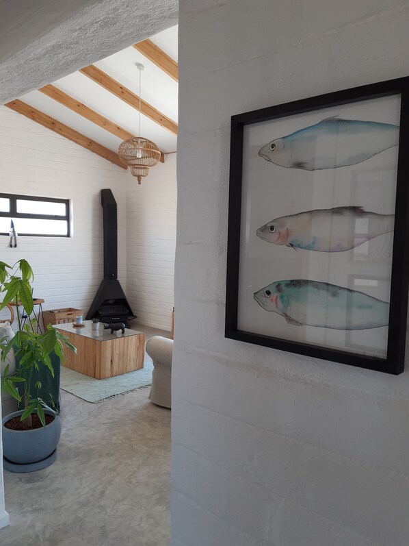 A modern living room with a fireplace, a large window, and a framed fish artwork on the wall.