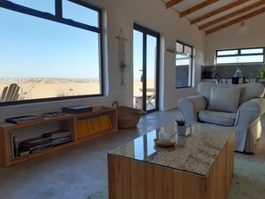 A spacious living area with a large window offering a desert view, a cozy sofa, a coffee table, and a bookshelf.