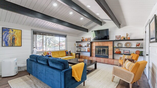 A living room with a blue sofa, yellow cushions, a fireplace, and a television on the wall. - Stunning 3 bedroom Sedona Home (Sedona)