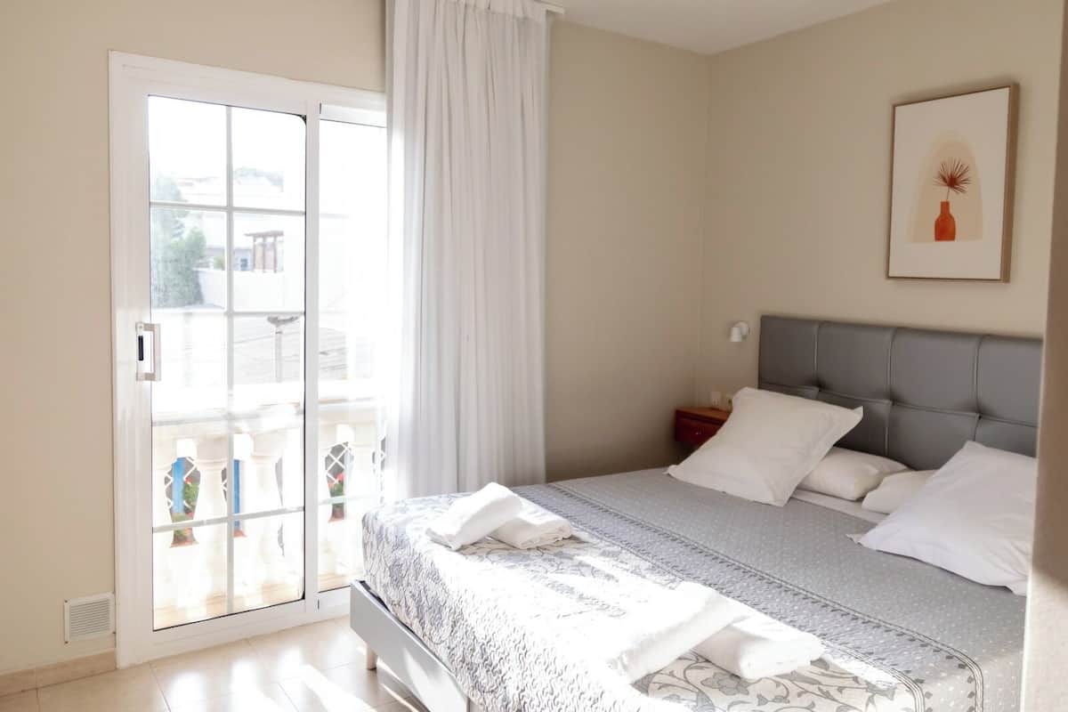 A bedroom with a bed, a nightstand, a window with curtains, and a framed picture on the wall.