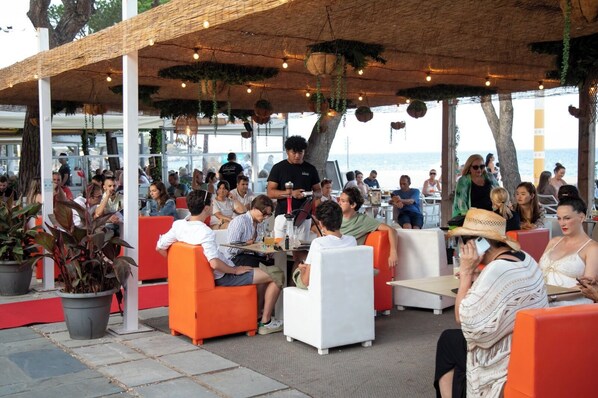 An outdoor seating area with orange and white chairs, potted plants, and hanging planters. - Hotel Serenity Platja D’Aro (Castell-Platja d'Aro)
