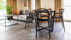 Una sala de estar moderna con una mesa de comedor y sillas, un sofá y un gran ventanal con cortinas.