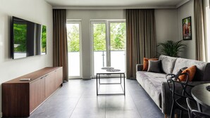 Una sala de estar moderna con un sofá, una mesa de centro, un televisor montado en la pared y un ventanal corredero que da a un balcón.