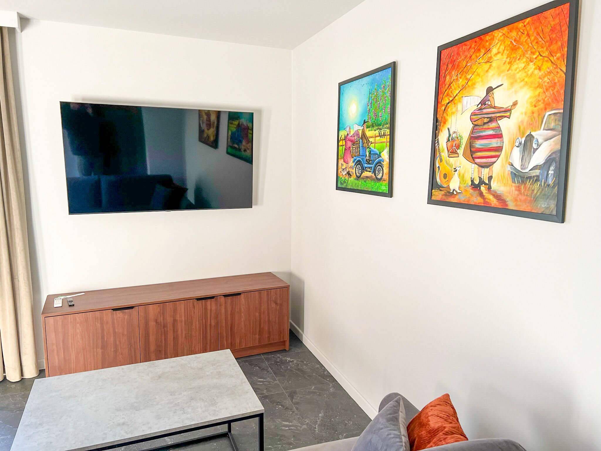 Un salon moderne avec un téléviseur à écran plat, un meuble en bois et deux tableaux aux couleurs vives accrochés au mur.