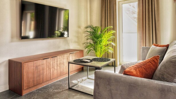 Una sala de estar moderna con un aparador de madera, una mesa de centro de vidrio, un sofá gris y un televisor de pantalla plana grande montado en la pared.