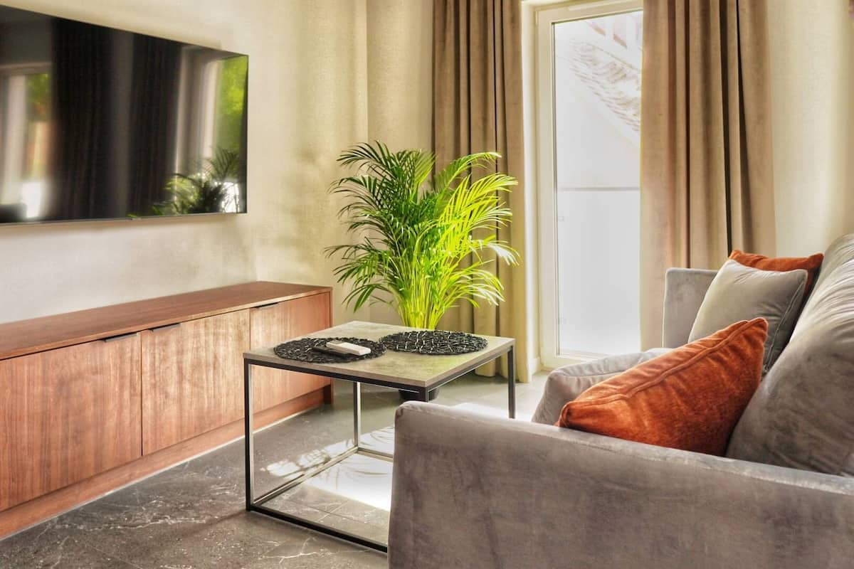 Een moderne woonkamer met een houten kast, een glazen salontafel, een grijze bank en een grote flatscreen televisie aan de muur.