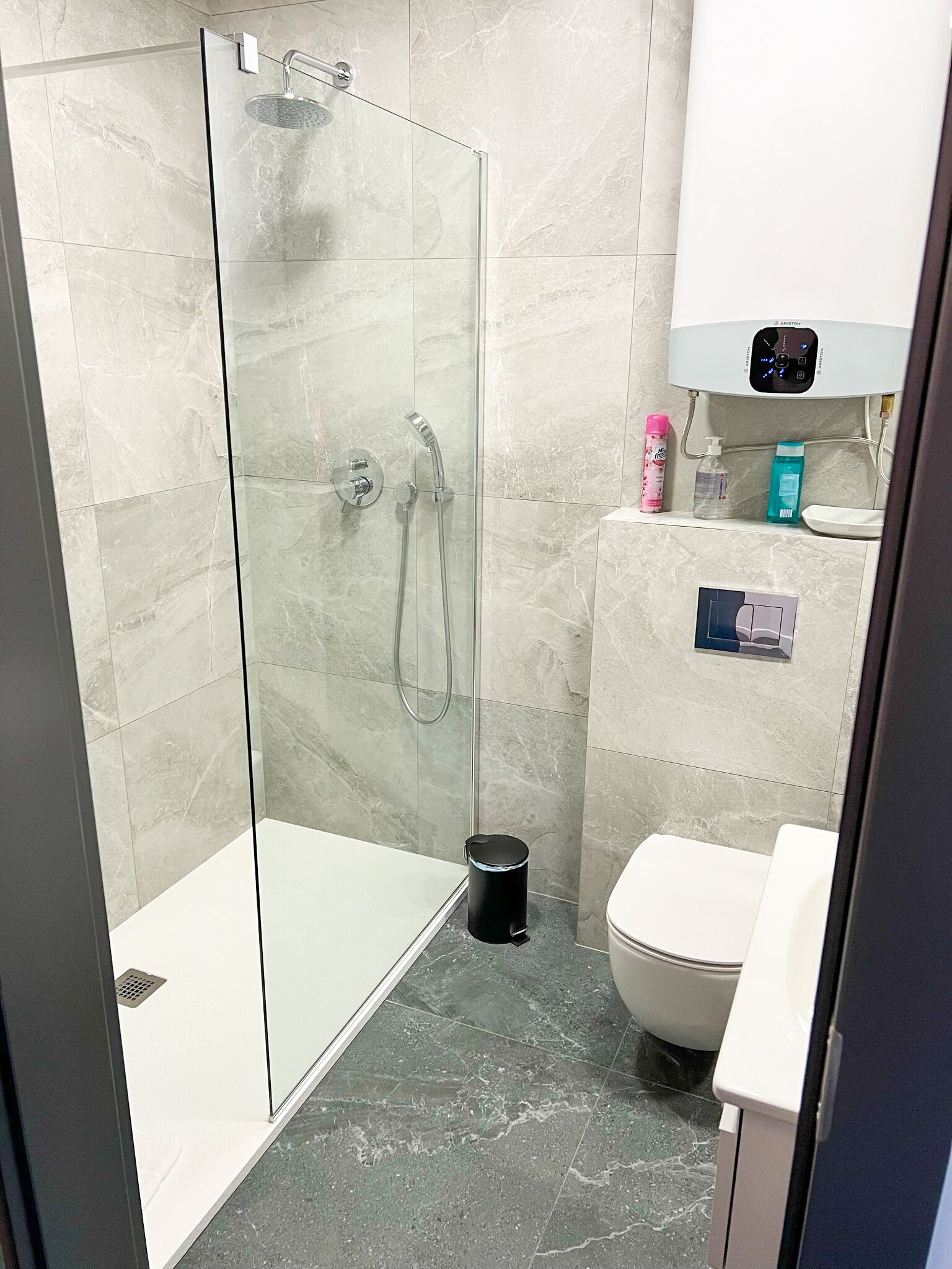 Un baño moderno con ducha de vidrio, inodoro y lavamanos con artículos de aseo.