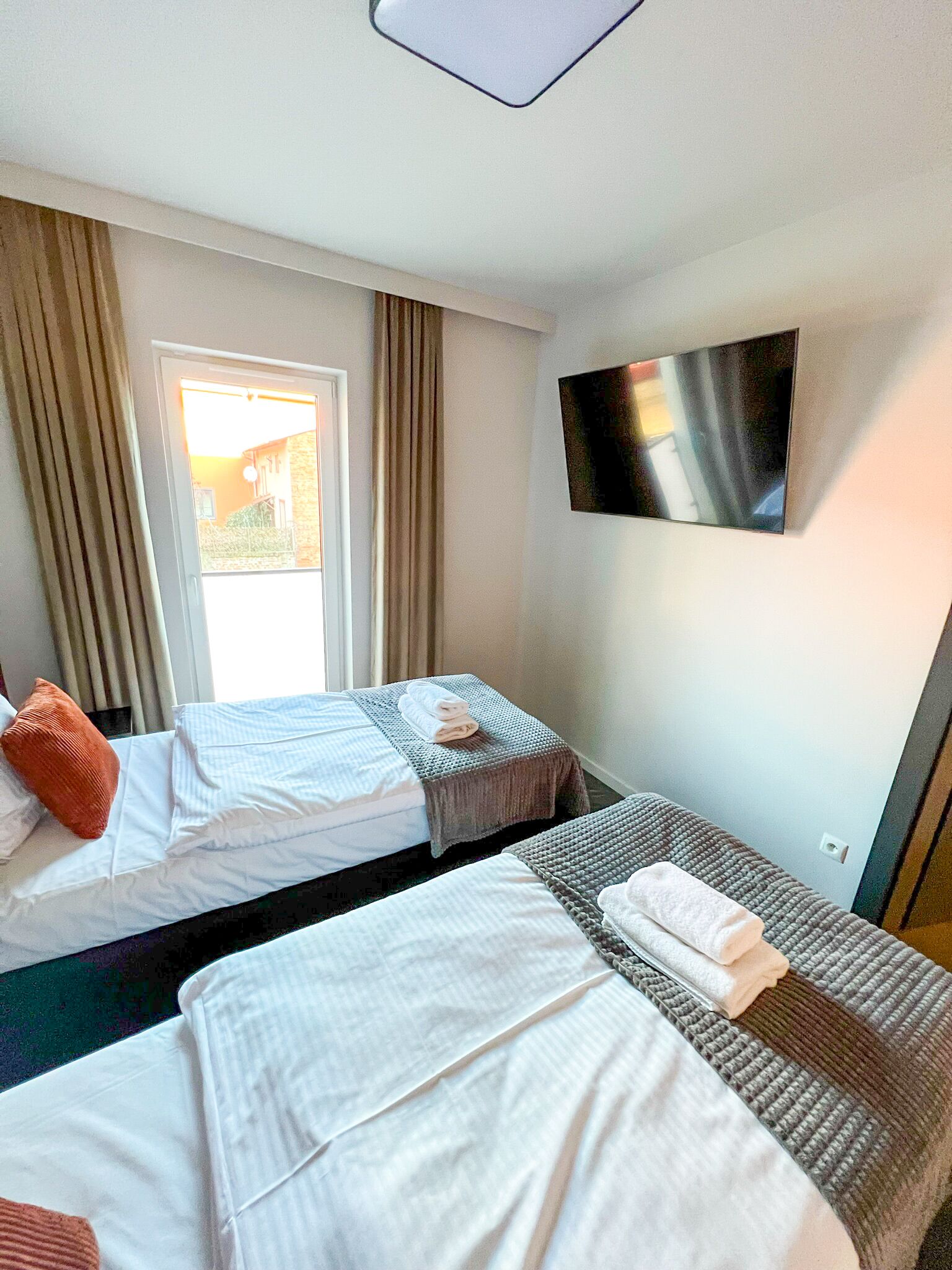 A hotel room with two beds, a TV on the wall, and a window with curtains.